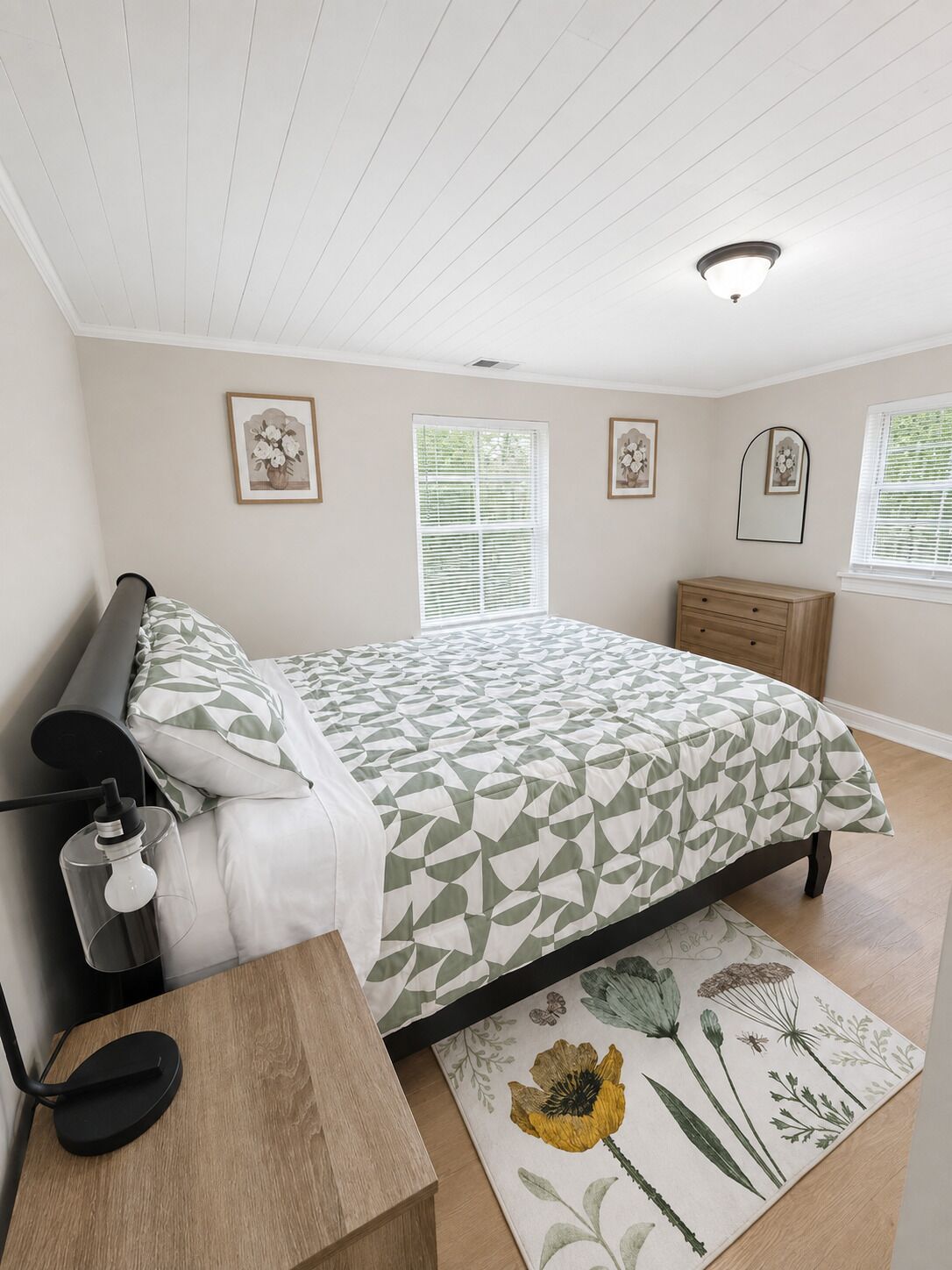 A bedroom with a bed, bedside tables, a lamp, a window with blinds, and framed pictures on the wall.