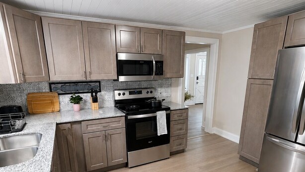 A modern kitchen with wooden cabinets, stainless steel appliances, and a granite countertop. - The Stone House • 5 Min to JMU • Fenced Yard • Peaceful Retreat No Neighbors (Harrisonburg)