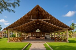 Eine große, offene Pavillon mit einem Reetdach, umgeben von Palmen und einem gepflegten Rasen.