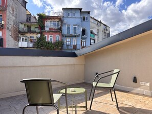 Eine Dachterrasse mit zwei Stühlen und einem kleinen Tisch, mit Blick auf eine Reihe bunter Häuser.