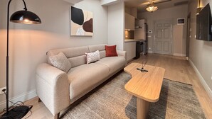 A modern living room with a sofa, a coffee table, and a lamp. There is a painting on the wall and a door leading to the kitchen. - Penthouse Suite with Private Terrace (Istanbul)