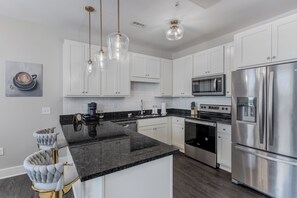 Una cocina moderna con armarios blancos, un refrigerador de acero inoxidable, un horno empotrado y una cafetera.