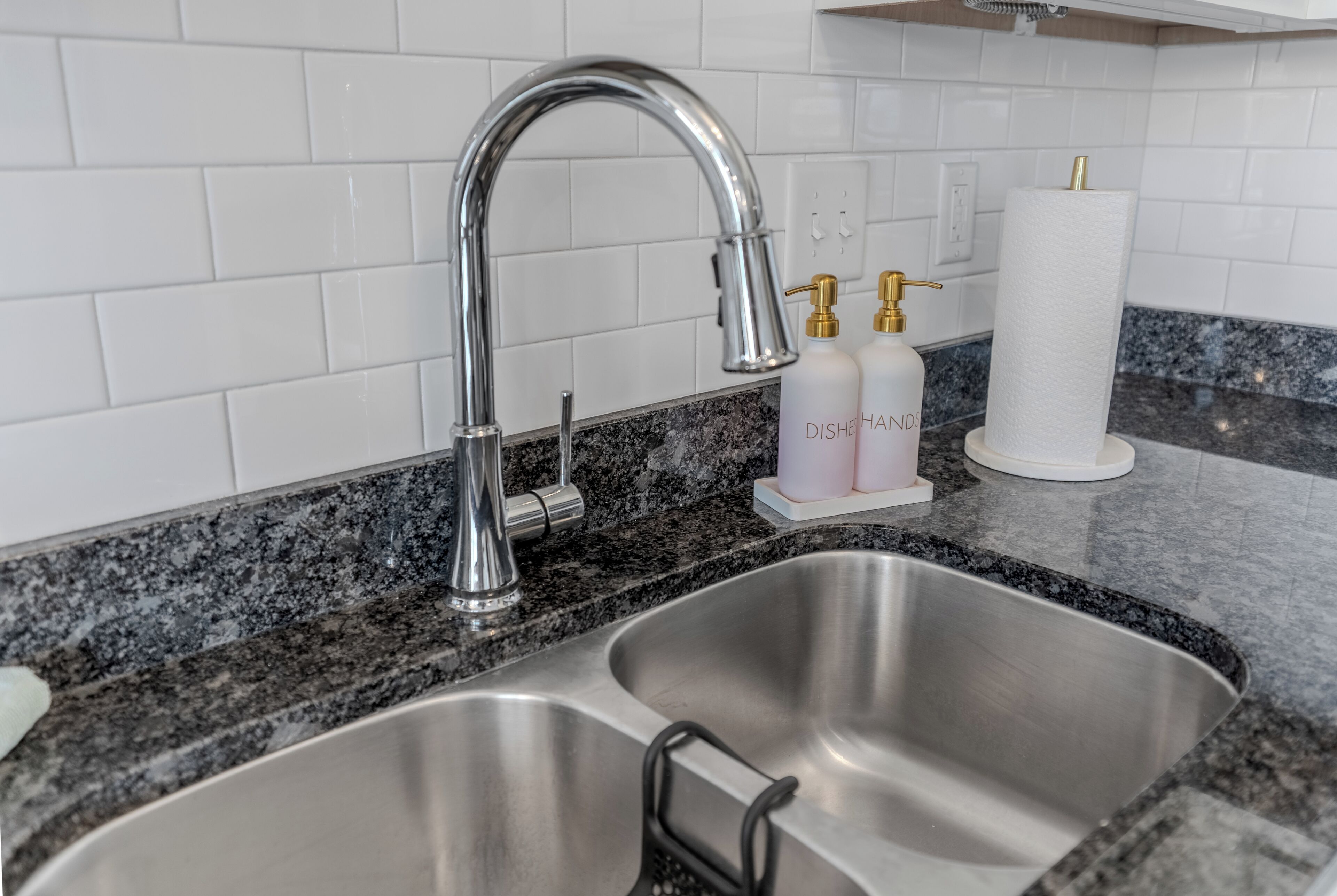 Un lavamanos de acero inoxidable con un grifo moderno, encimera de granito y un dispensador de toallas de papel con un rollo.