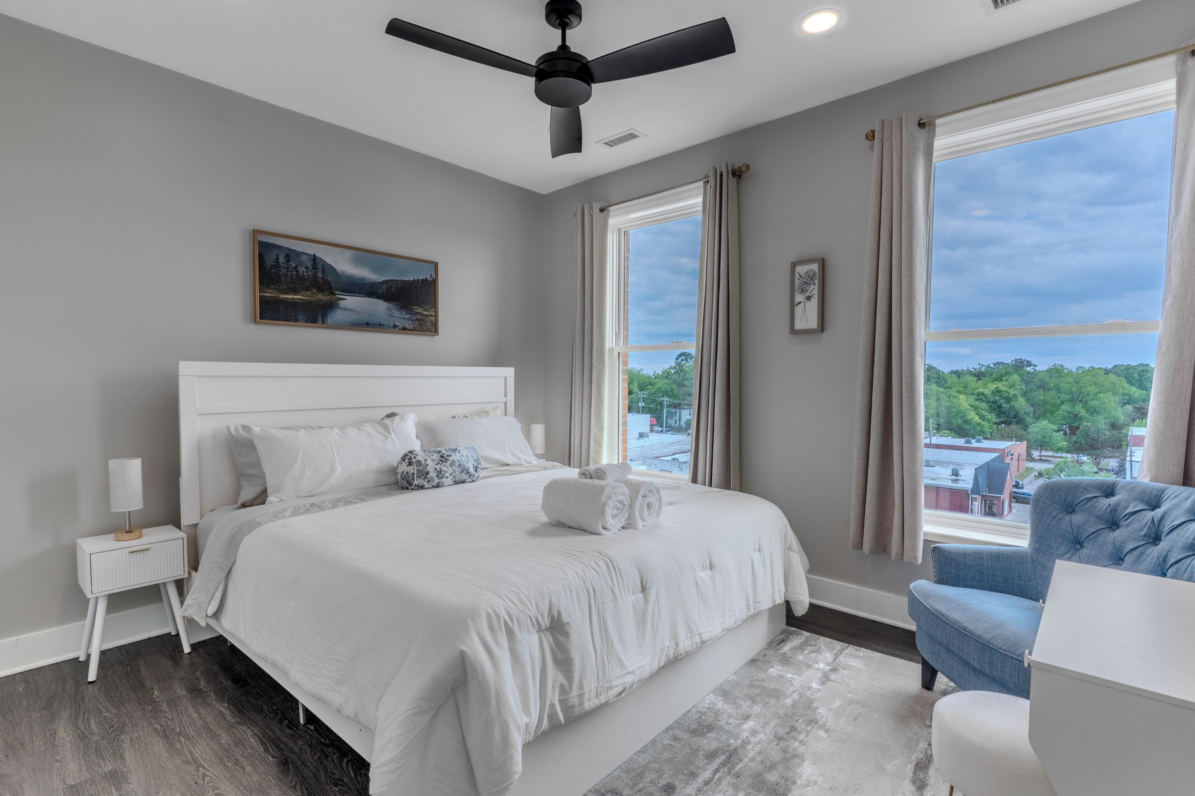 A bedroom with a bed, a nightstand, a chair, a ceiling fan, and a window with curtains.