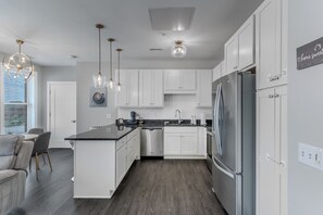 A modern kitchen with white cabinetry, a stainless steel refrigerator, and pendant lighting.