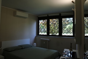 Ein Schlafzimmer mit einem Bett, einem Heizkörper, einem Fenster mit Blick auf Bäume und einer Lampe.