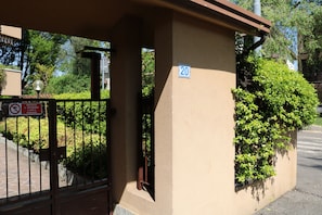 Ein begrenzter Zugang mit einem Schild 'Keine Motorräder', ein Gebäude mit der Aufschrift '20' und ein gepflegter Heckenstreifen.