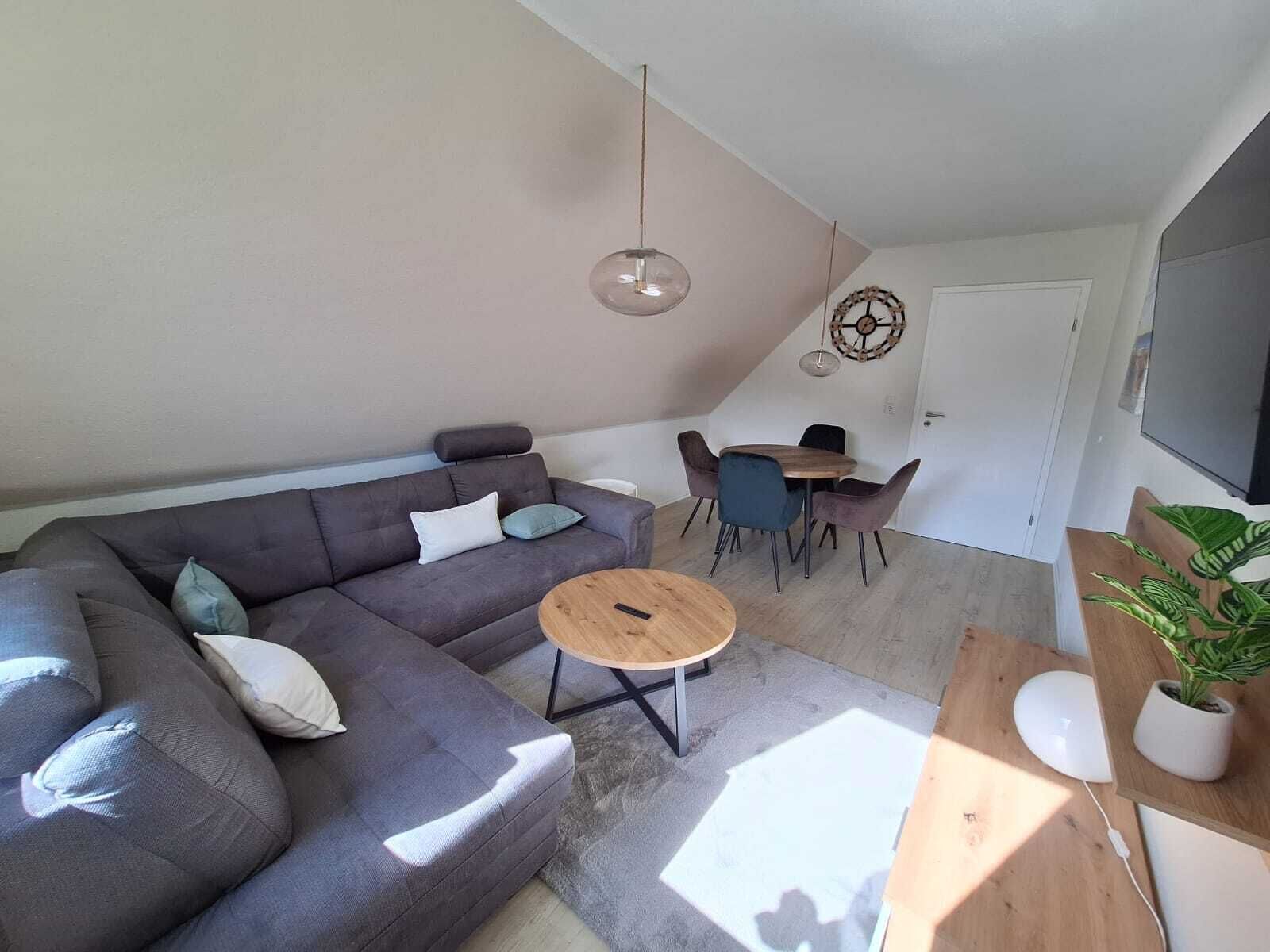 Et moderne opholdsrum med en grå sofa, et rundt sofabord og et spiseområde med stole.