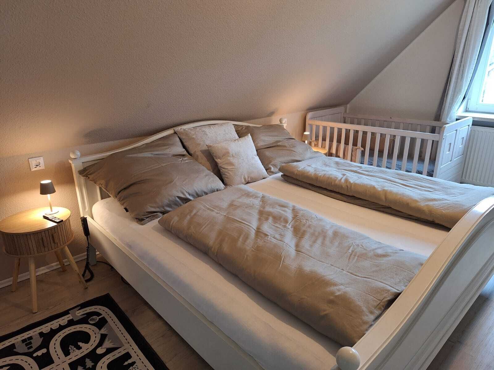 Ein Einzelbett mit weißem Gestell und beiger Bettwäsche in einem Zimmer mit geneigter Decke und einem Fenster.