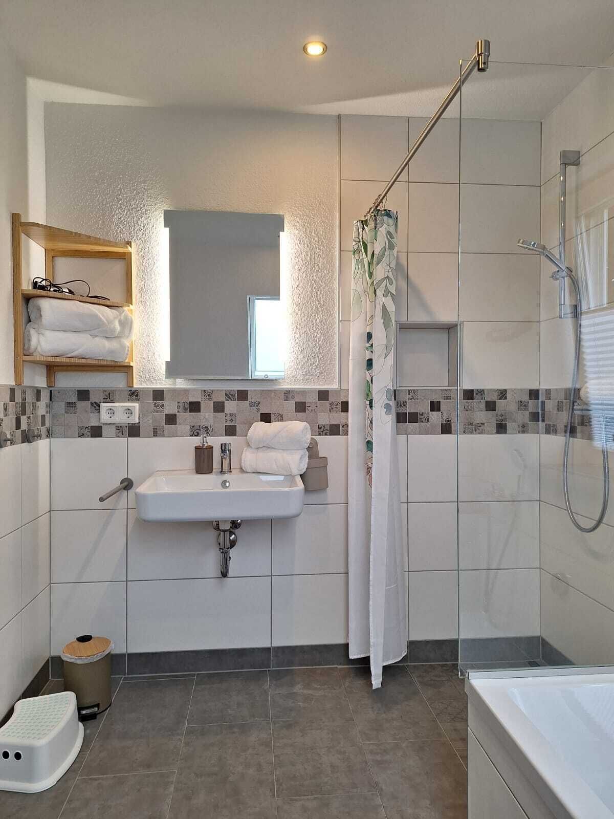 Ein modernes Badezimmer mit Waschbecken, Spiegel, Dusche und einer kleinen Stufe.