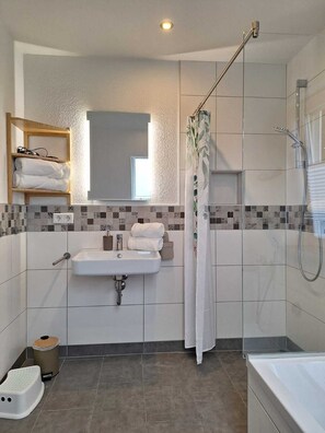 A modern bathroom with a sink, mirror, shower, and a step stool. - Modern, child-friendly vacation rental not far from the North Sea (Langenhorn)
