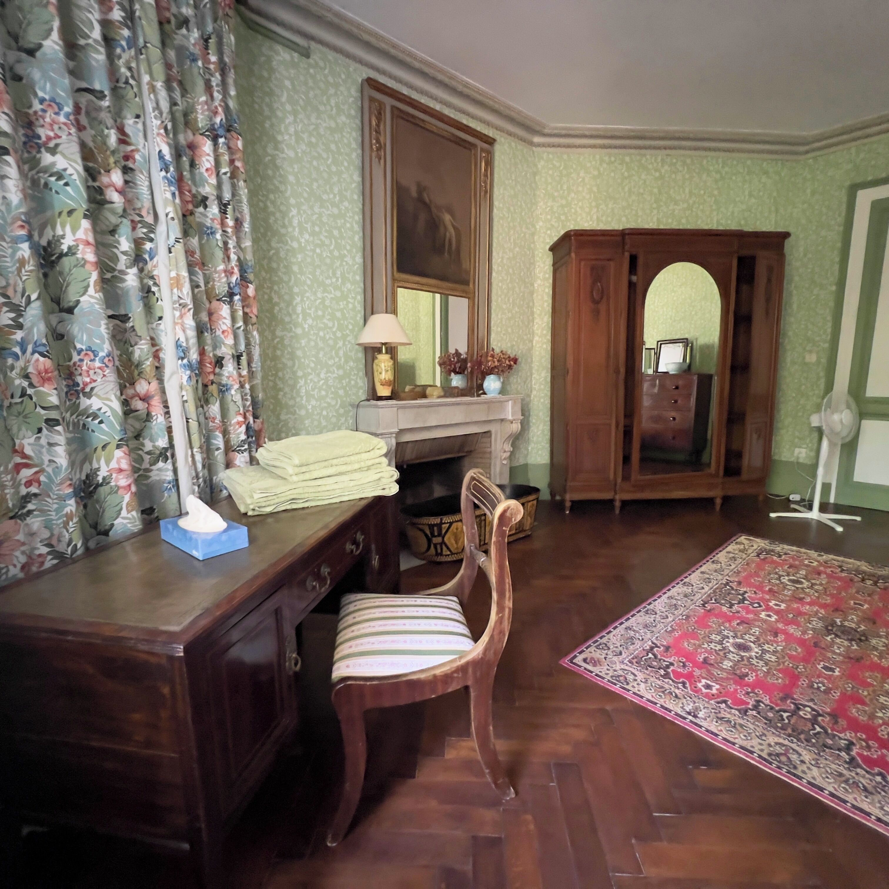 A room with a wooden desk, a chair, a mirror, a cabinet, and a patterned rug.