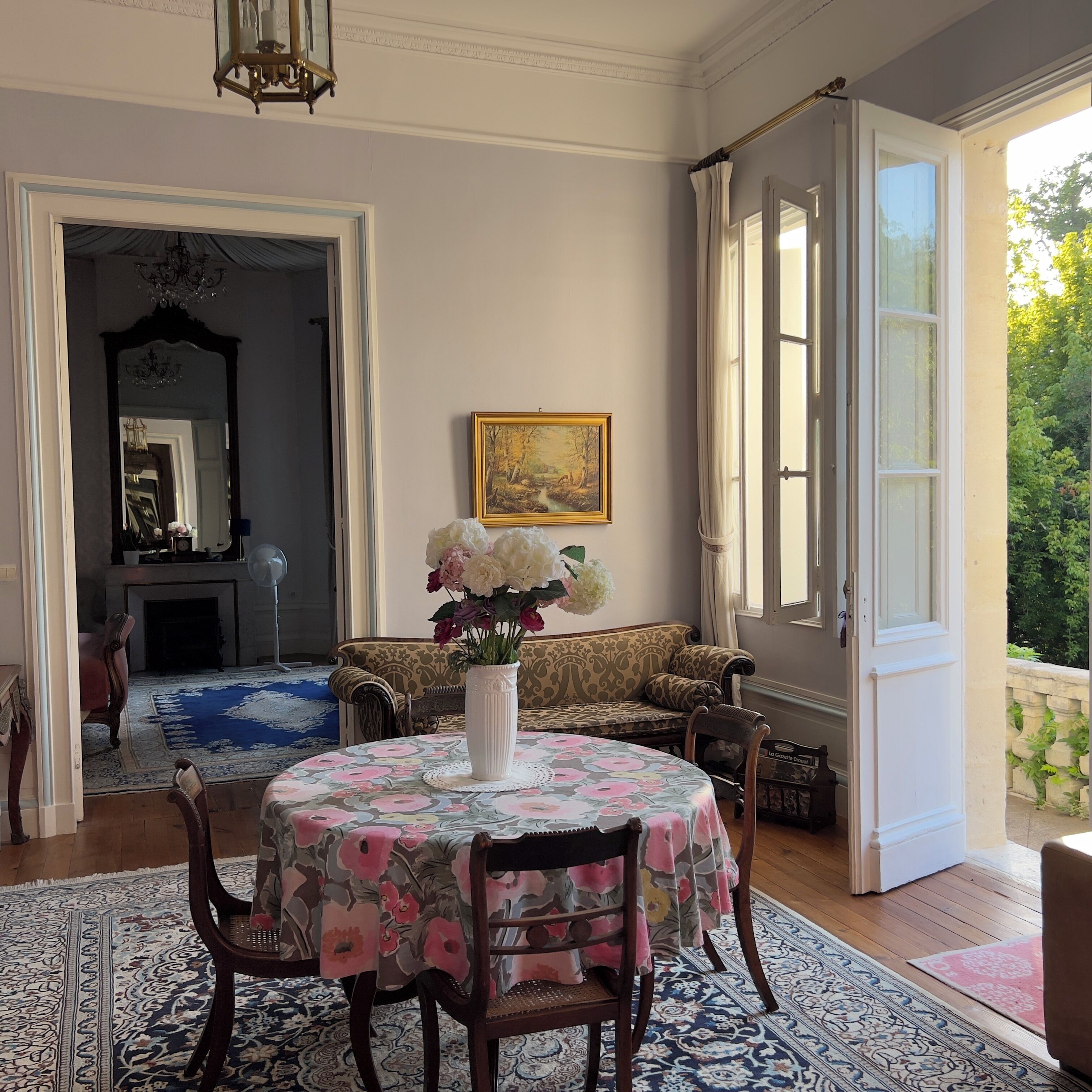 Una habitación con una mesa redonda, sillas, un sofá, un cuadro y una ventana con cortinas.
