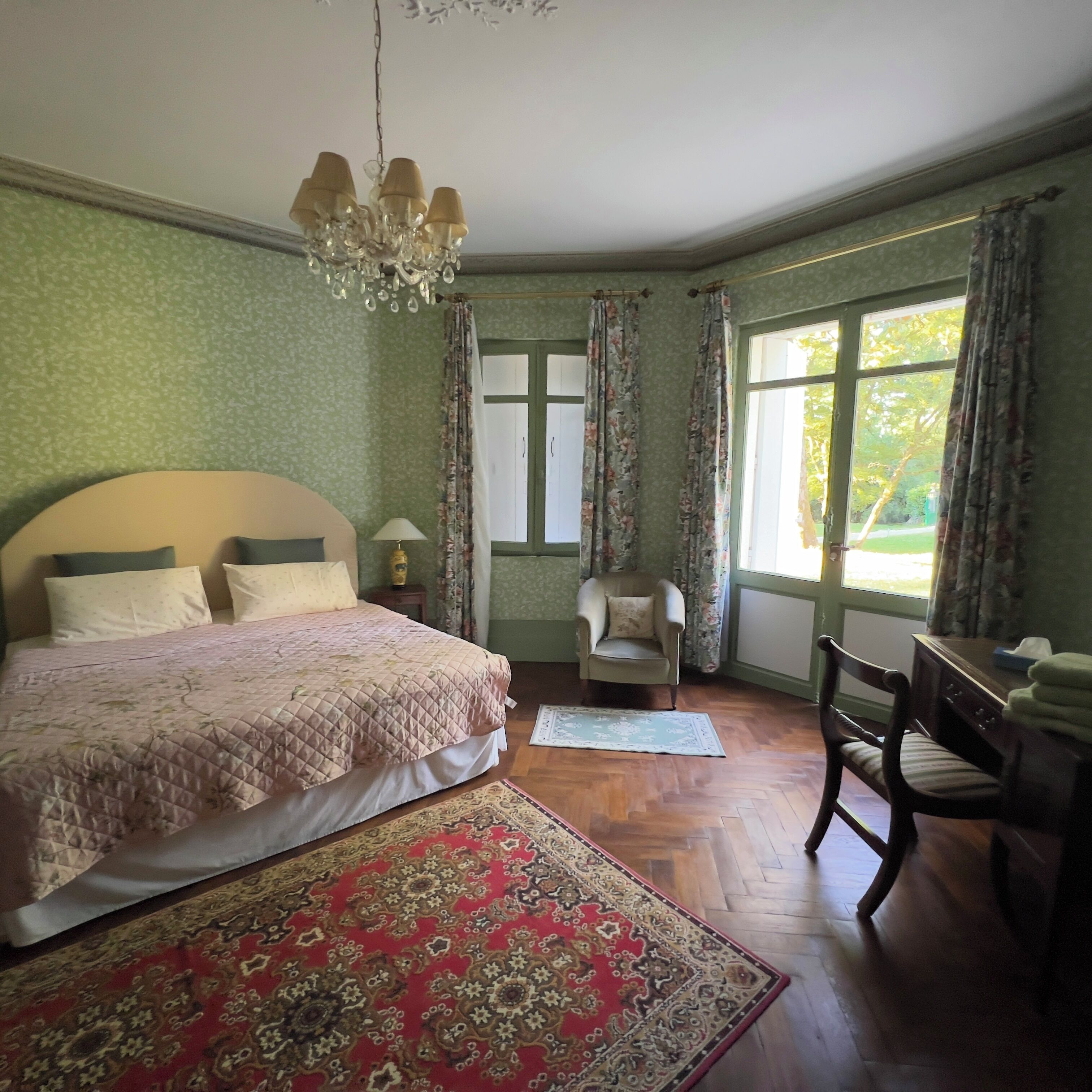 A bedroom with a large bed, a chair, a desk, and a window.