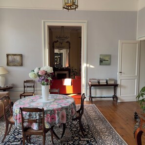 A dining area with a round table, chairs, a vase with flowers, a chandelier, and a view into another room. - Superb 4-bedroom Chateau in a private setting of 4 hectares of woodland. (Coutras)