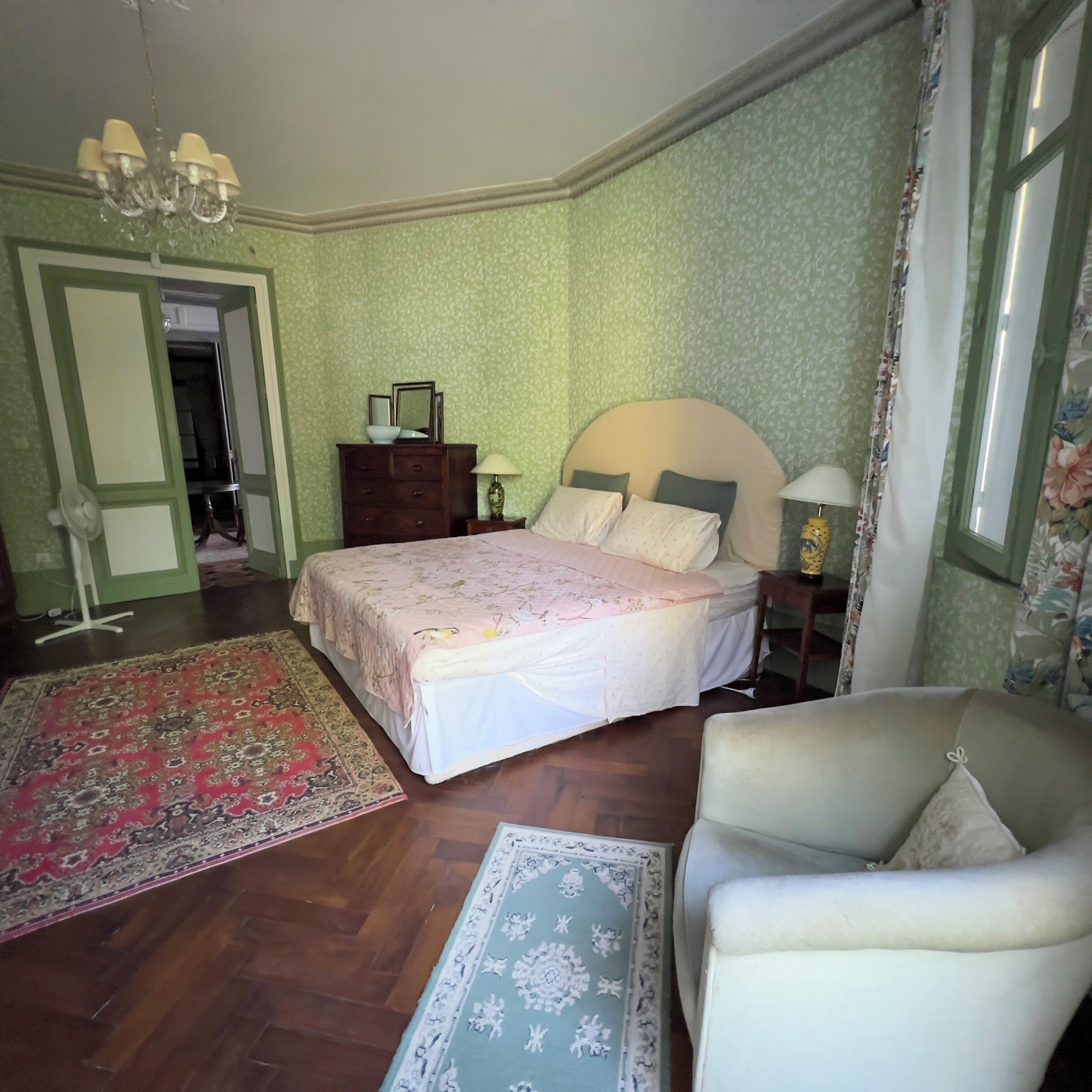 A bedroom with a bed, a chair, a dresser, a lamp, and a chandelier.