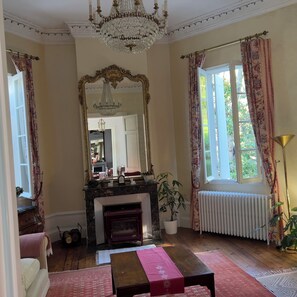 A room with a fireplace, a mirror, a chandelier, and a window with curtains. - Superb 4-bedroom Chateau in a private setting of 4 hectares of woodland. (Coutras)