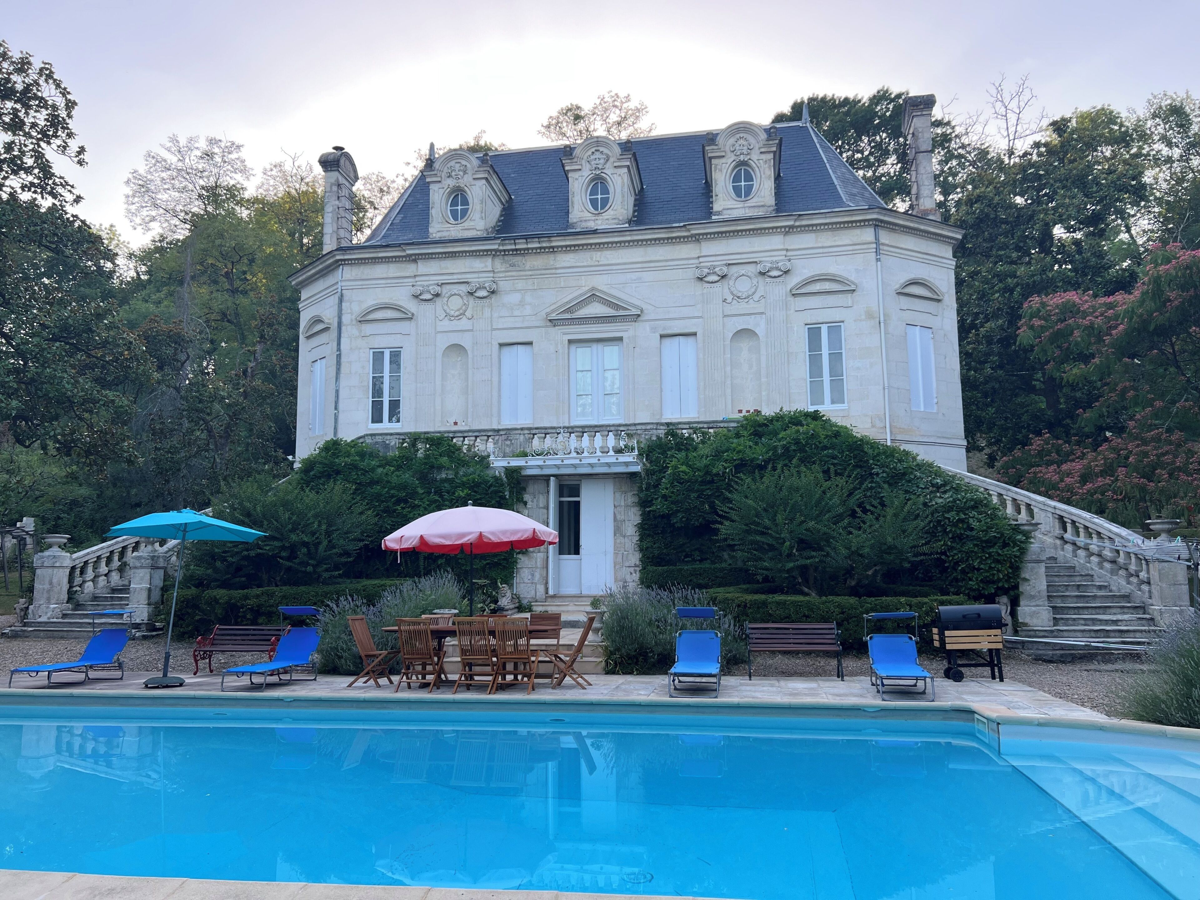 A large building with a swimming pool, outdoor seating, and a staircase leading to the entrance.