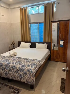 Een hotelkamer met een bed, gordijnen, een houten garderobe en een raam met uitzicht.