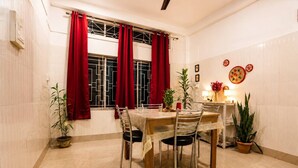 A dining area with a table set for four, red curtains, potted plants, and wall decorations.