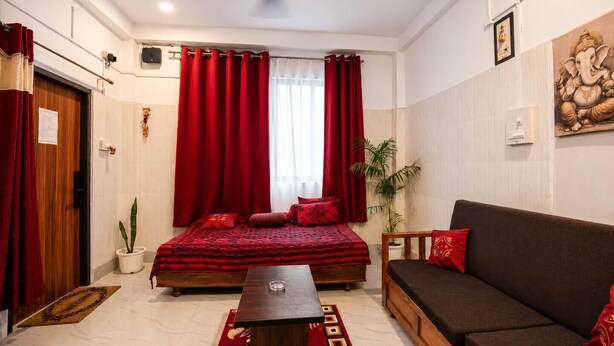 A room with a bed, a sofa, a small table, a potted plant, and a ceiling fan.