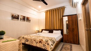 A hotel room with a bed, a bedside table, a mirror, a ceiling fan, and a window with curtains.