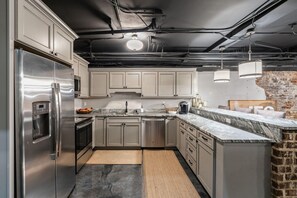 A modern kitchen with stainless steel appliances, marble countertops, and a brick accent wall. - Historic Loft, Downtown Knoxville, Market Square (Knoxville)