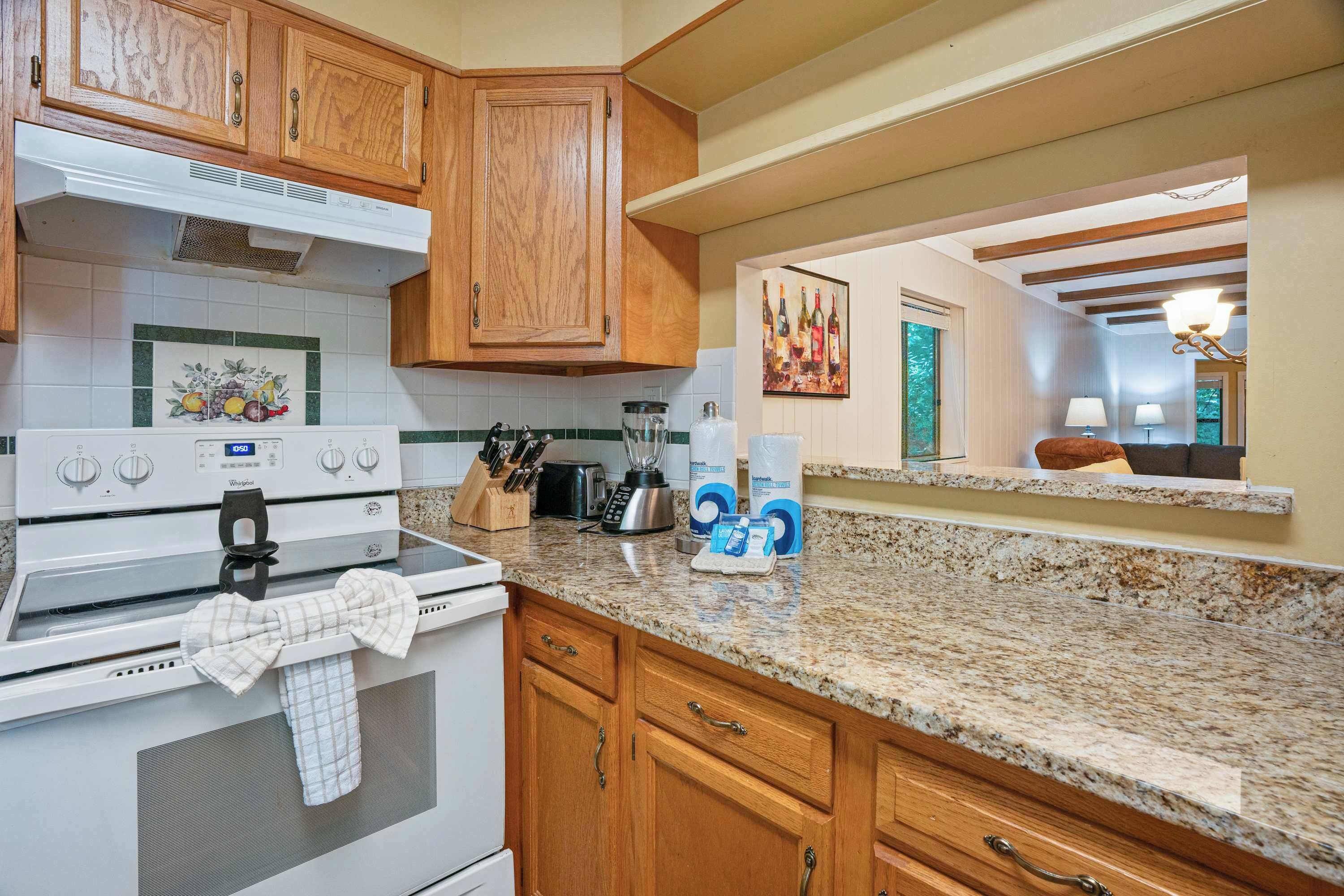 A kitchen with wooden cabinets, a Whirlpool stove, a granite countertop, and a painting of wine bottles on the wall.