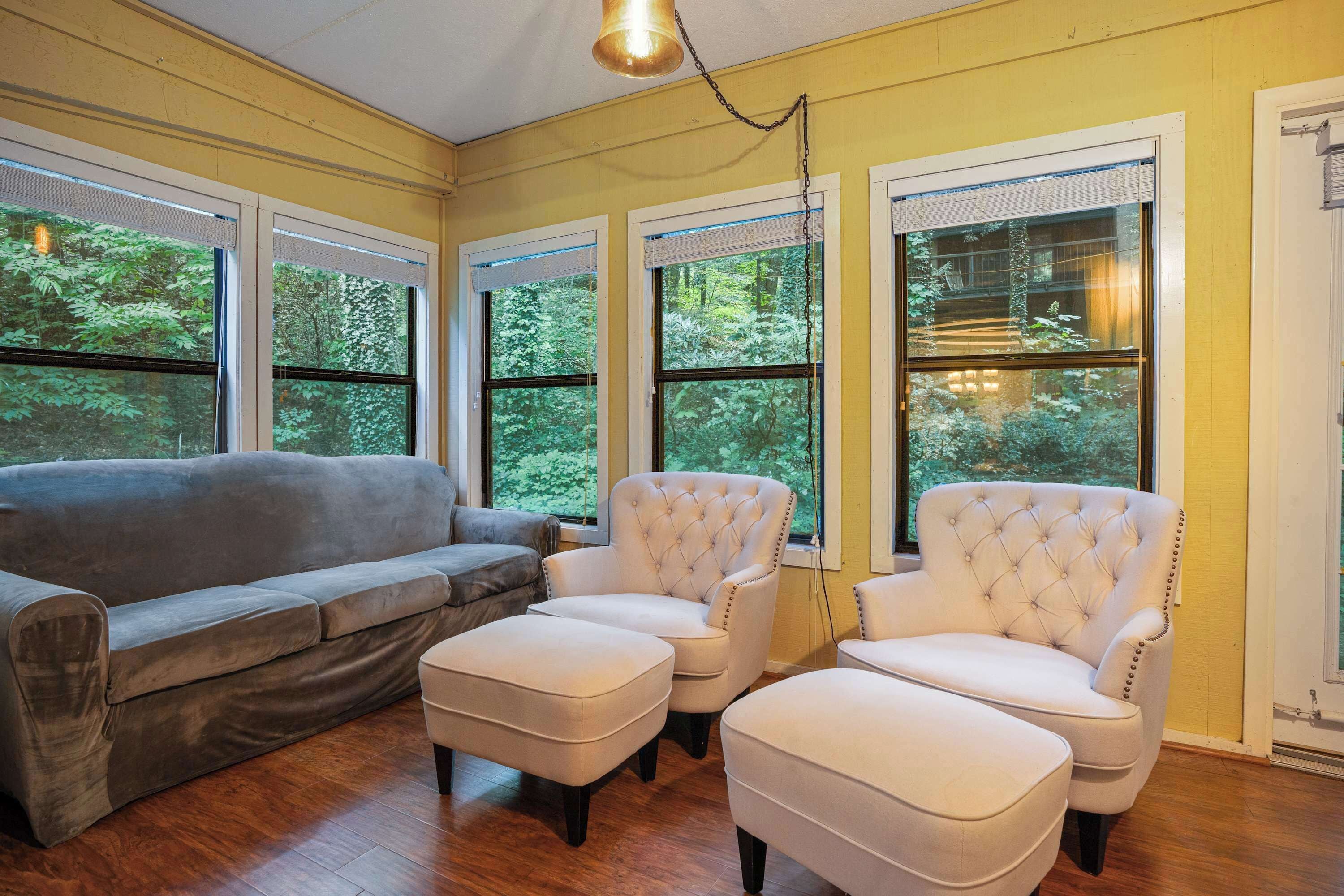 A room with a gray sofa, two white armchairs, and a wooden floor.