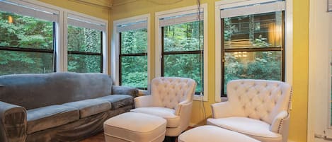 A room with a gray sofa, two white armchairs, and a wooden floor.