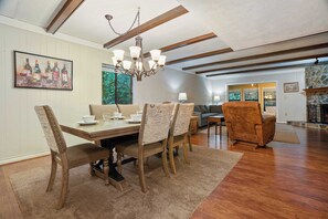 A dining area with a wooden table, chairs, and a chandelier. There is a painting on the wall and a sofa in the background. - Bright Sunroom, Wooded Views, Ober Mountain Base (Gatlinburg)