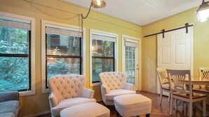 A room with two white armchairs, a wooden dining table, and a view of a forest through large windows. - 3BR Condo Near Ober Mountain & Downtown Gatlinburg (Gatlinburg)