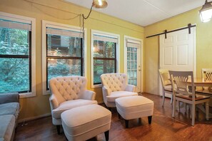 A room with two white armchairs, a wooden dining table, and a view of a forest through large windows. - 3BR Condo Near Ober Mountain & Downtown Gatlinburg (Gatlinburg)