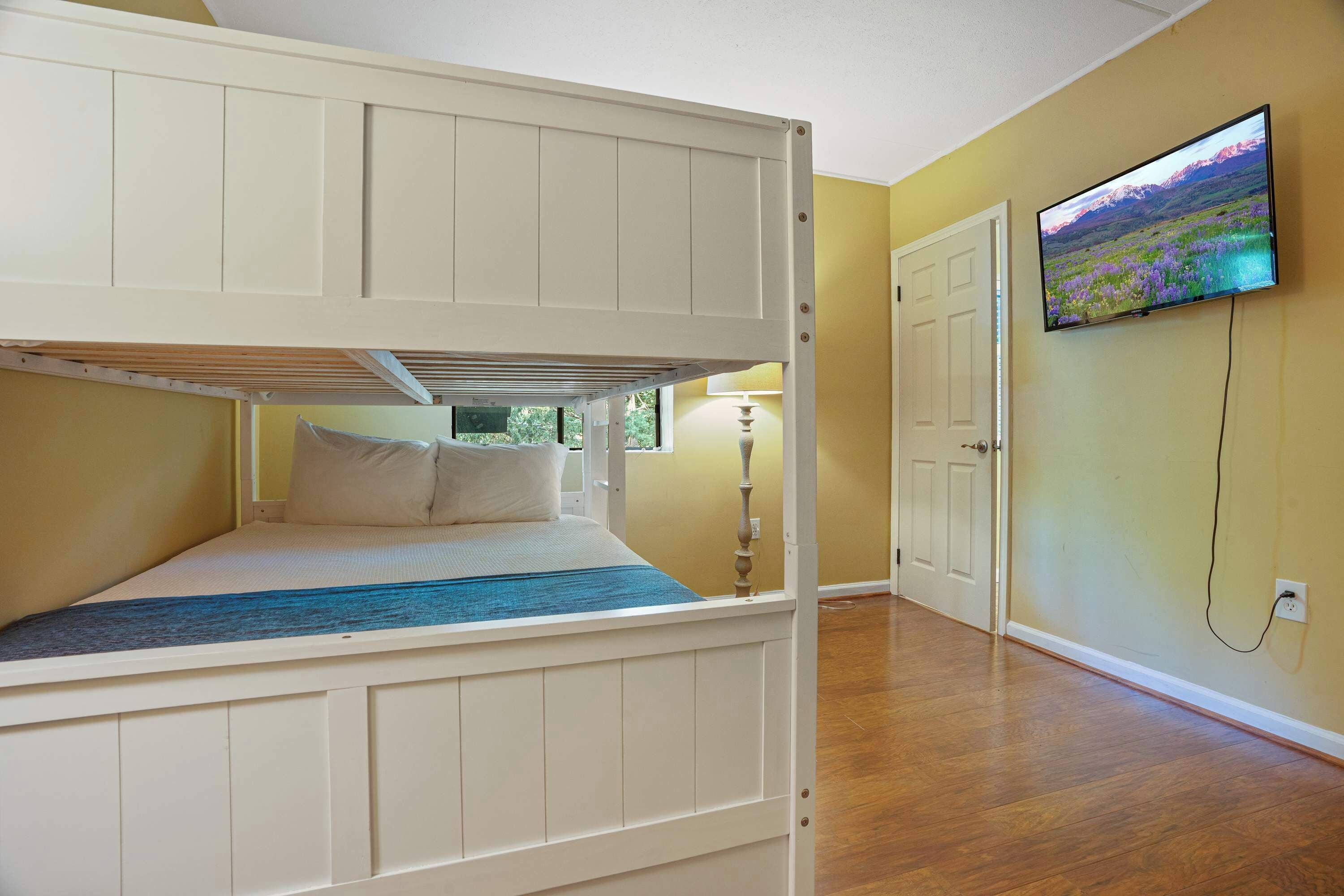 A room with a bunk bed, a television mounted on the wall, and a door leading to another room.
