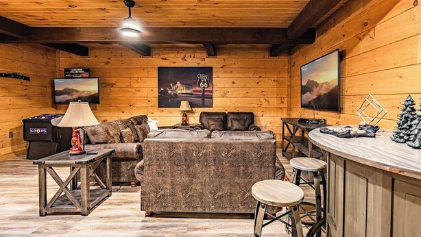 Ein gemütliches Blockhauss-Interieur mit einer Couch, einer Bar und einem Fernseher, der ein Landschaftsbild zeigt.