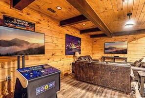 Ein Blockhaus-Interieur mit Spielkonsole, einer Couch und Wand-Fernsehern.