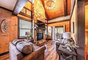 A cozy cabin interior with a stone fireplace, wooden walls, and a comfortable seating area. - 4BR Smoky Mountain Cabin, Hot Tub & Theater (Sevierville)