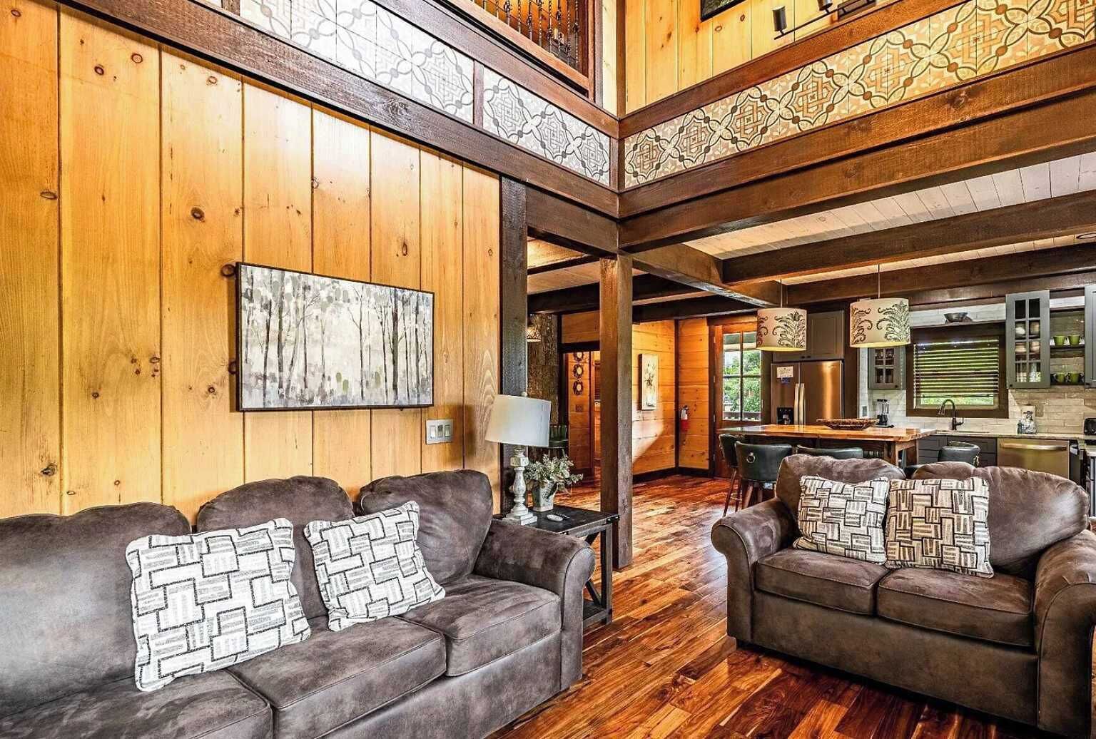 A spacious living area with wooden paneling, a dining table, and two sofas with patterned cushions.