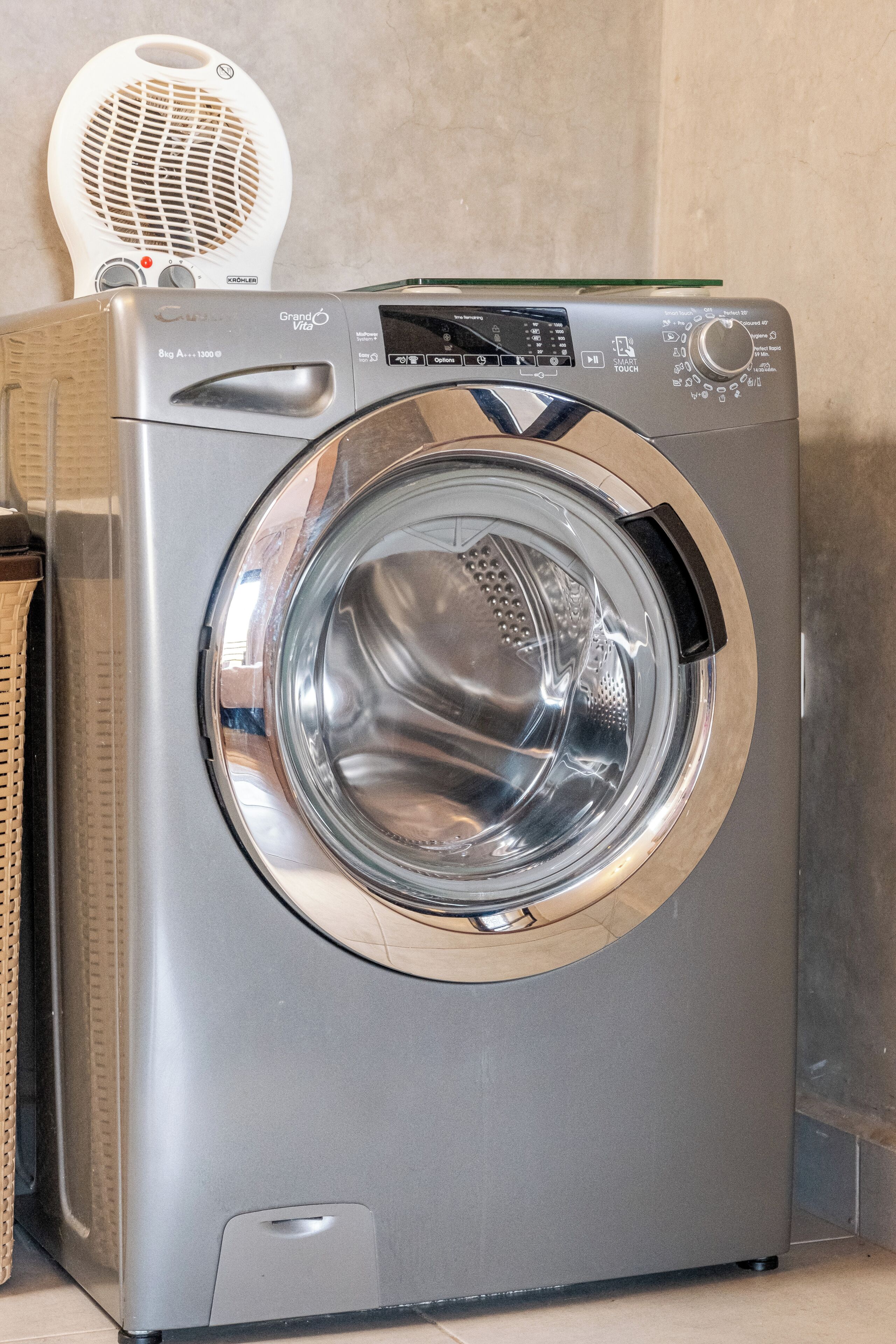 Voorzijde van een compacte, moderne wasmachine met een digita bedieningspaneel, een transparante deur en een klein, rond ventilatierooster bovenop.