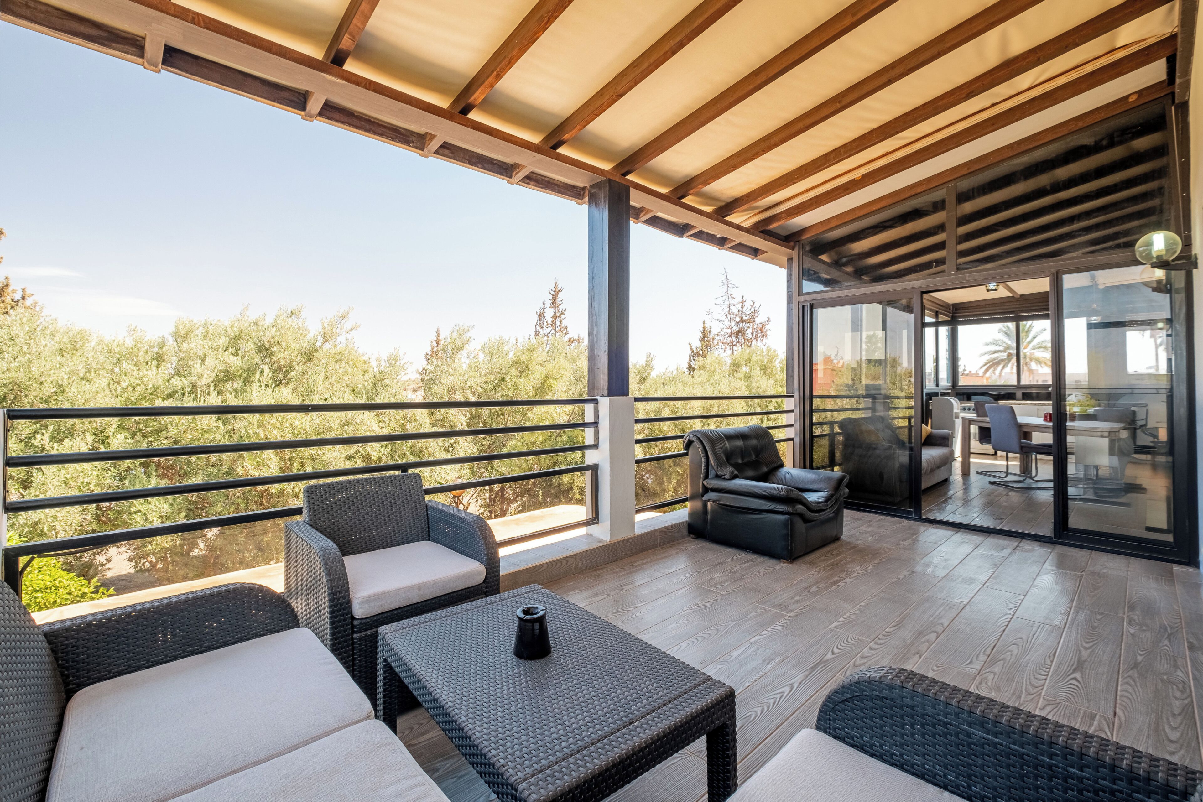 An outdoor patio with wicker furniture, a view of trees, and a glass door leading to an indoor area.