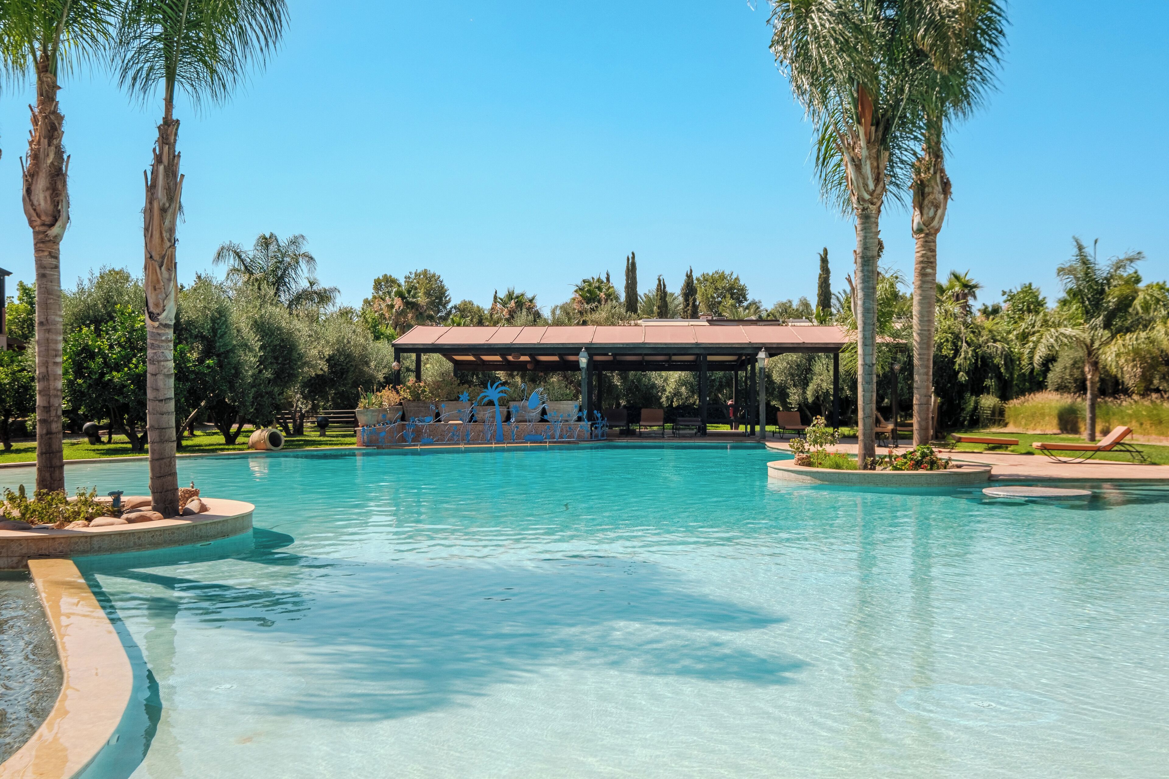 Une piscine d’un bleu éclatant, dotée d’un espace de repos abrité et bordée de palmiers.