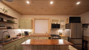 Una cocina con una isla de madera, gabinetes verdes, un refrigerador de acero inoxidable y una ventana con persianas.