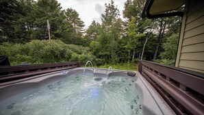 Un jacuzzi con banca de madera y barandilla de madera, rodeado de vegetación exuberante y árboles.