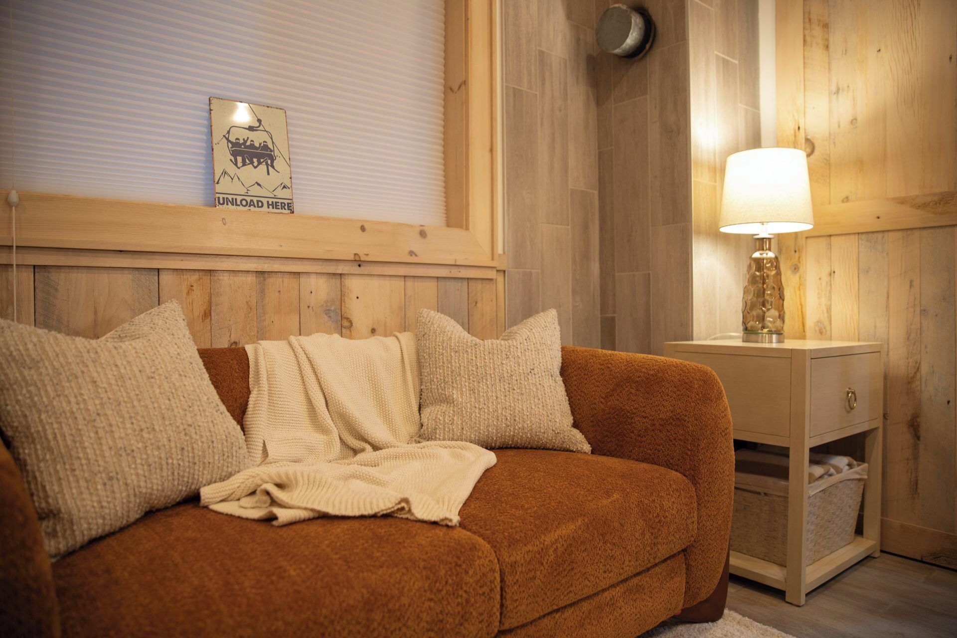 A cozy room with a brown sofa, a white lamp, and a wooden wall.