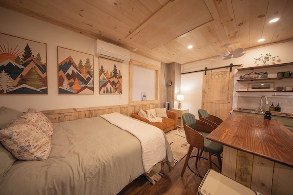 Una habitación acogedora con una cama, una mesa de comedor de madera y una zona de cocina.