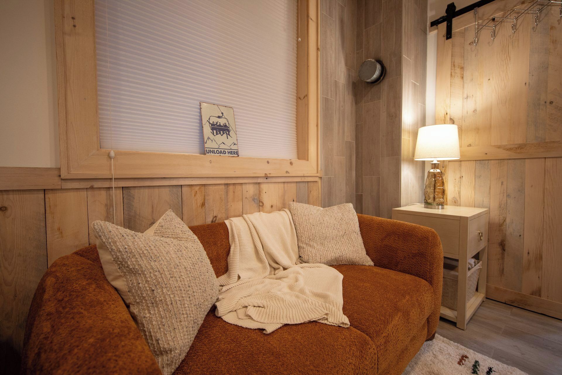 Una habitación acogedora con un sofá marrón, una manta blanca de punto y una pared de madera.