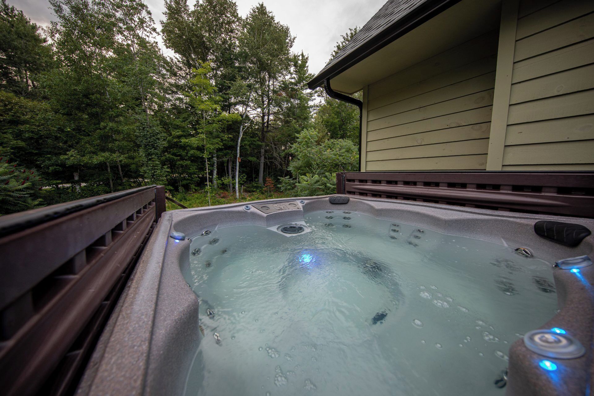 A hot tub with a wooden deck and a house in the background.