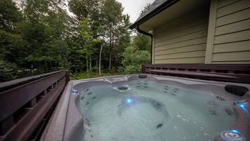 A hot tub with a wooden deck and a house in the background.