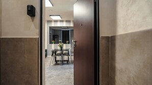 A hallway with a door leading to a room with a table and chairs, a potted plant, and a wall-mounted light fixture. - Termini Jacuzzi Suite (Roma)