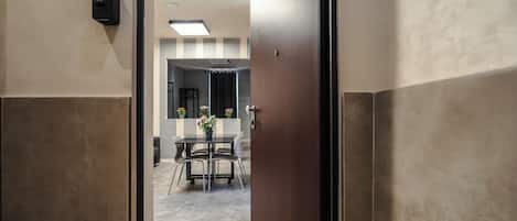 A hallway with a door leading to a room with a table and chairs, a potted plant, and a wall-mounted light fixture.